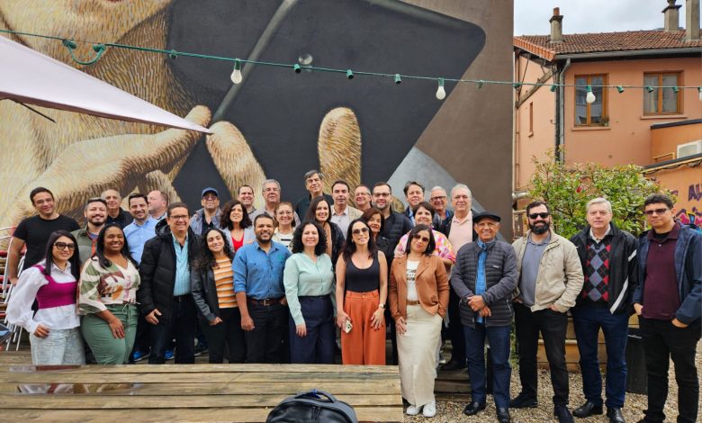 Integrantes da 'Missão Raízes do Cooperativismo' posam para uma foto em frente a uma obra de arte urbana durante sua visita à cooperativa Les Relais Solidaires em Paris, destacando o intercâmbio cultural e a aprendizagem em sua jornada pelo conhecimento cooperativo