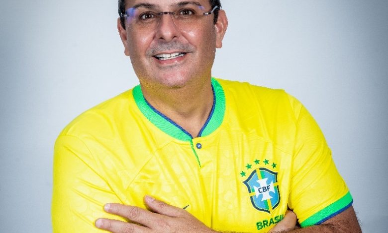 o candidato a prefeito de itaguaí alexandre valle, vestindo uma camisa da seleção brasileira de futebol, está com os braços cruzados e sorrindo