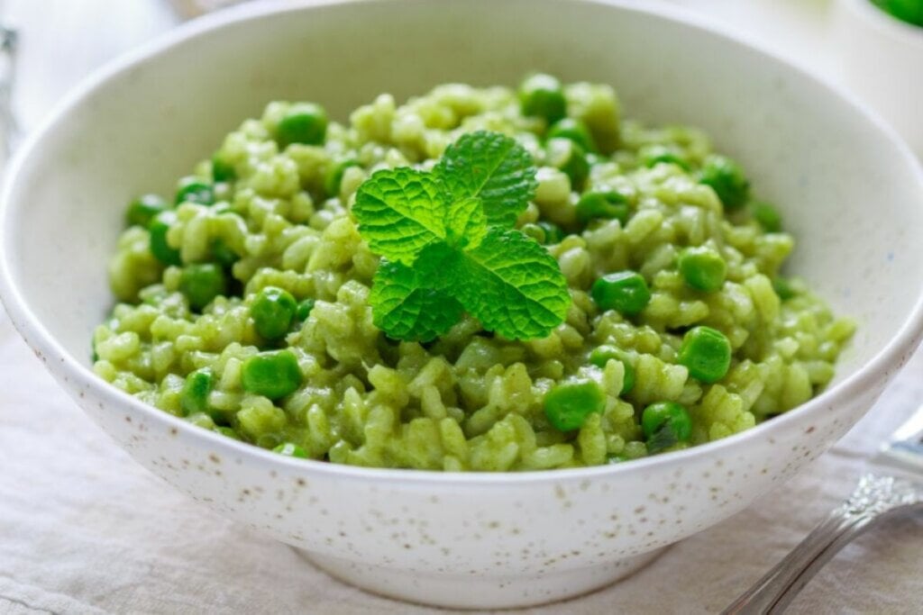 Arroz cremoso com ervilha decorado com folhas de manjericão em um recipiente branco