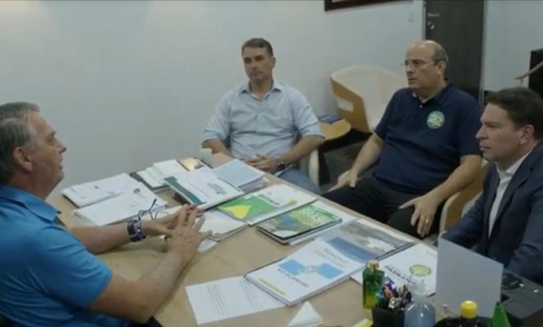 Em uma mesa de escritório, Alexandre Valle, Jair Bolsonaro, Flávio Bolsonaro e Alexandre Ramagem conversam.