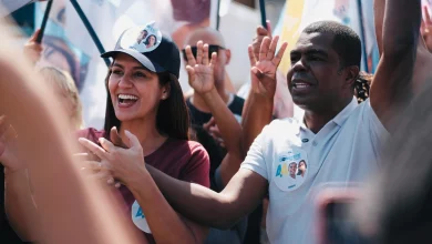 Donizete com Ana Sagário, em meio a bandeiras, fazem campanha em uma rua de Itaguaí