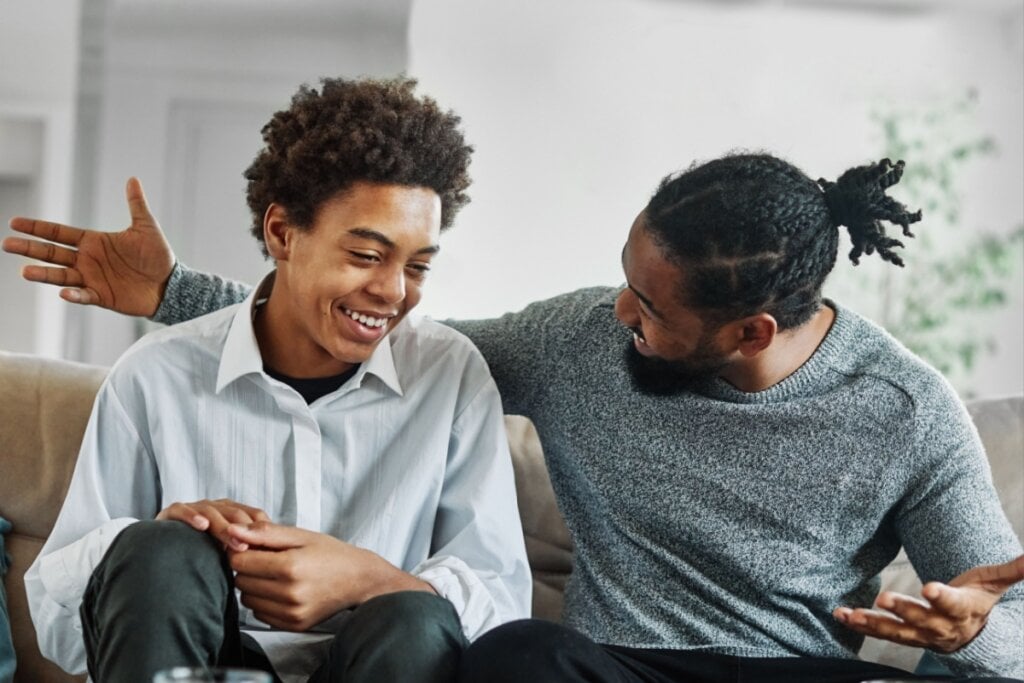 Jovem menino e um homem sentado em um sofá conversando e sorrindo 