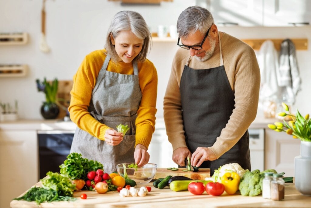 mulher e homem idosos picando verduras em cozinha