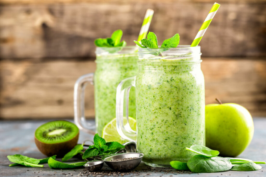 Vitamina verde em caneca de vidro. Ao lado, kiwi, maçã, espinafre e semente de chia