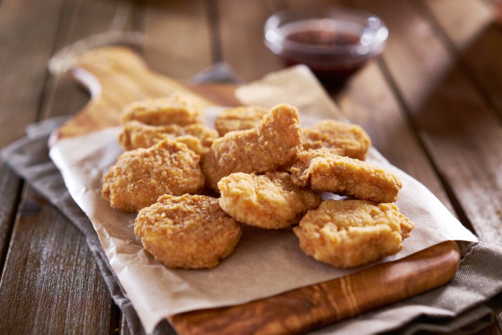 Nuggets assados em cima de tábua de carne sobre pano cinza 