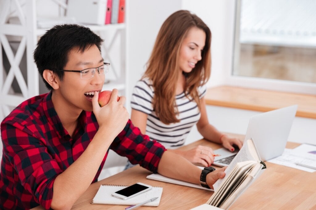 Homem sentado ao lado de uma mulher estudando e comendo maçã 