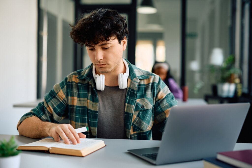 Estudante lendo livro e usando notebook