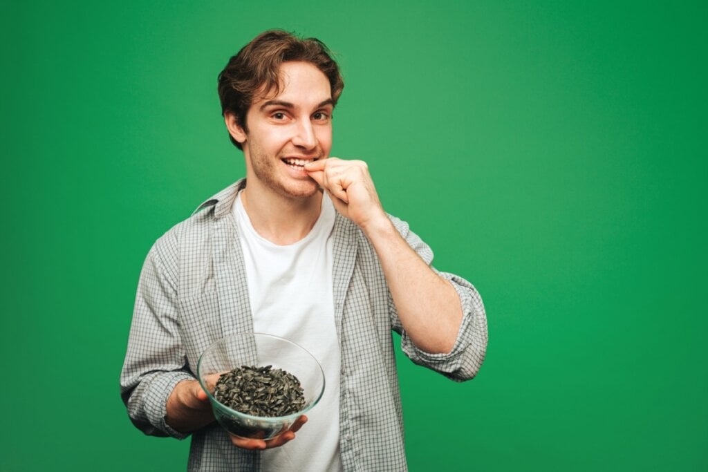 Homem fazendo gesto de colocar alimento na boca e segurando recipiente com sementes de girassol