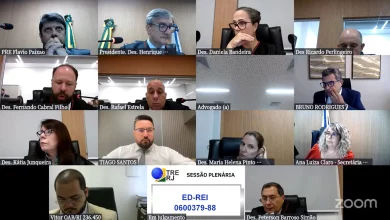 A imagem mostra uma sessão plenária virtual do Tribunal Regional Eleitoral do Rio de Janeiro (TRE-RJ), exibindo 12 participantes em uma videoconferência, com câmeras ligadas. Entre eles, há desembargadores, advogados e outros profissionais. Na parte superior da imagem, podemos ver nomes identificados nos quadros individuais, como **Flavio Paixão**, **Henrique**, **Daniela Bandeira**, **Ricardo Perlingeiro**, e outros. A legenda central inferior informa que a sessão é referente ao processo **ED-REI 0600379-88**, com o status "Em julgamento". A tela está dividida em quadrantes, com cada participante aparecendo em sua própria janela. Algumas pessoas parecem estar ouvindo com atenção, enquanto outras estão concentradas ou interagindo. No canto inferior direito, o ícone do **Zoom** sugere que a sessão está sendo transmitida via essa plataforma de videoconferência.