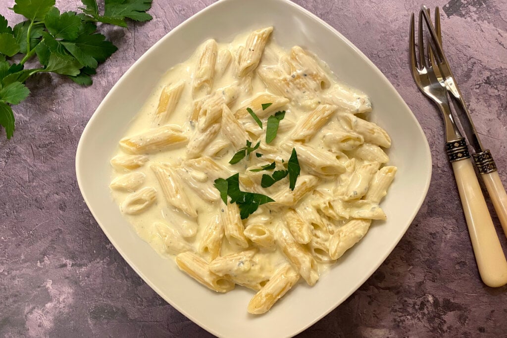 Prato com macarrão e creme de leite decorado com cheiro-verde e talheres ao lado