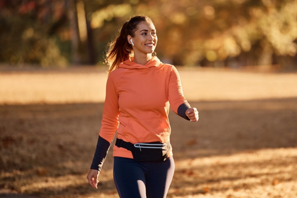 Mulher usando uma blusa de manga longa laranja, calça preta e uma pochete caminhando em um parque 