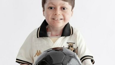 Gui, torcedor símbolo do Vasco indicado ao Prêmio Torcedor do Ano da FIFA, posa para foto de camisa clara e gola escura, segurando uma bola.