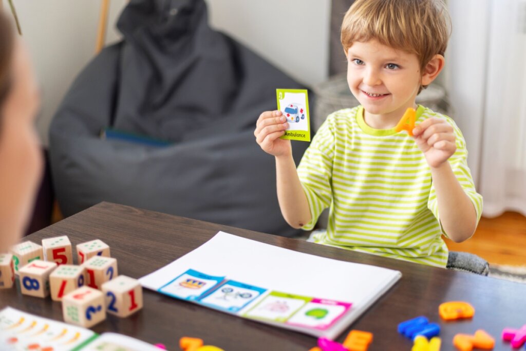 Menino sorrindo, segurando cartões educativos e letras coloridas