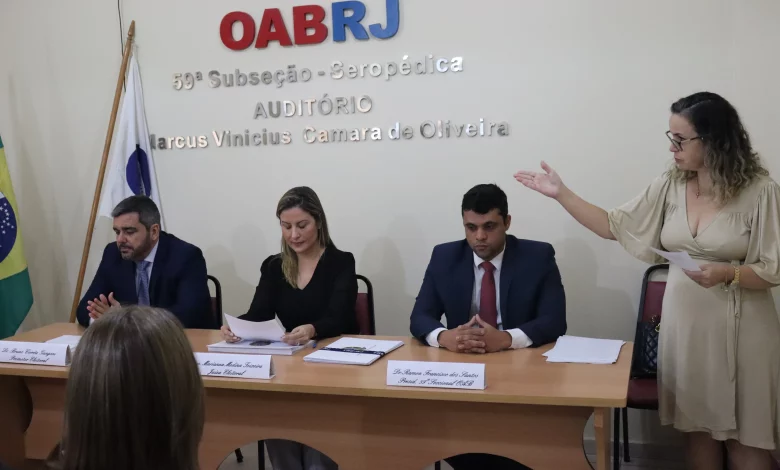 Mulher discursa ao lado de pessoas sentadas à mesa