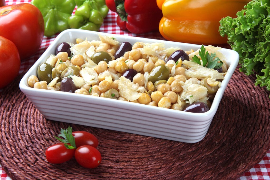 Recipiente branco com salada de grão-de-bico com bacalhau e azeitonas 