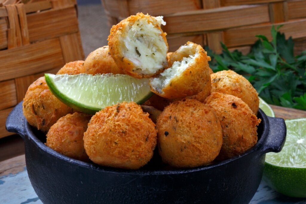 Bolinhos de bacalhau em uma cumbuca preta e com uma fatia de limão