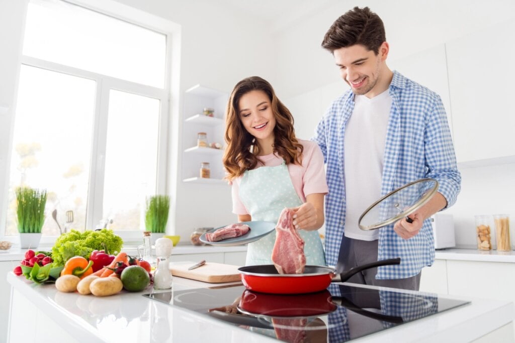 Casal cozinhando carne na cozinha