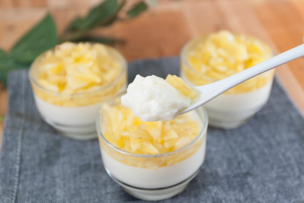 Doce com base branca e abacaxi em cima em recipiente de vidro