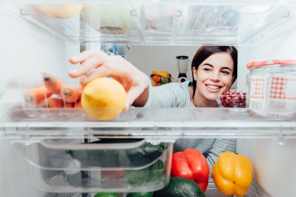 Mulher colocando uma fruta dentro da geladeira com vista de dentro do refrigerador