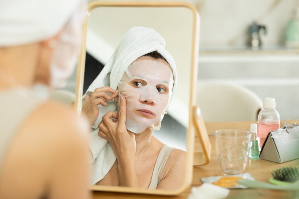 Mulher em frente a um espelho colocando uma máscara facial no rosto 