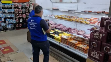 Fiscais da Vigilância Sanitária vistoriando balcão frigorífico de supermercado.