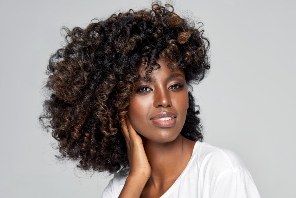 Mulher com cabelo marrom café usando uma blusa branca e posando para foto em frente a um fundo cinza 