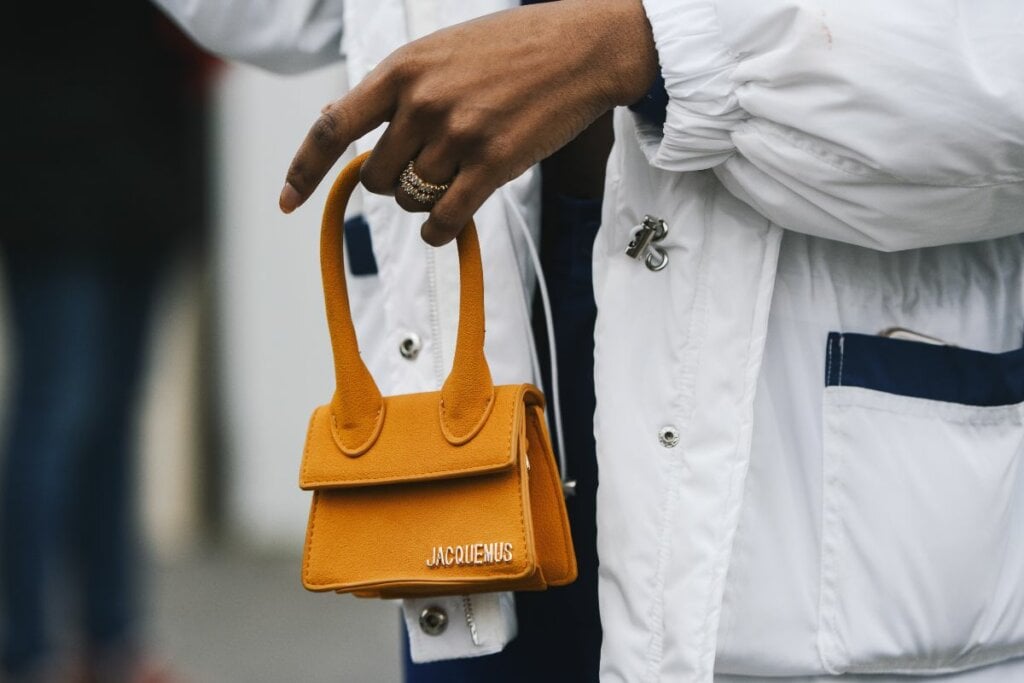 Mão feminina segurando uma micro bolsa laranja 