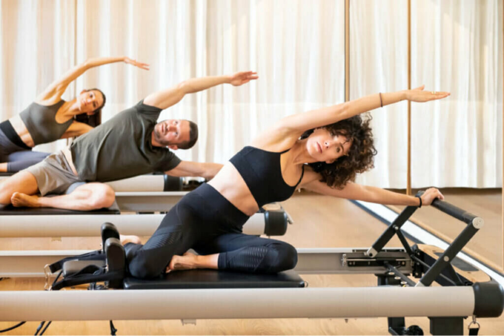 Duas mulheres e um homem fazendo pilates em cima do equipamento