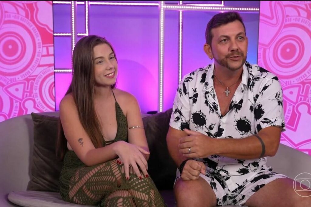 Raissa e Edilberto do BBB25 sentados em um sofá em frente a um fundo com luzes rosa e roxo 