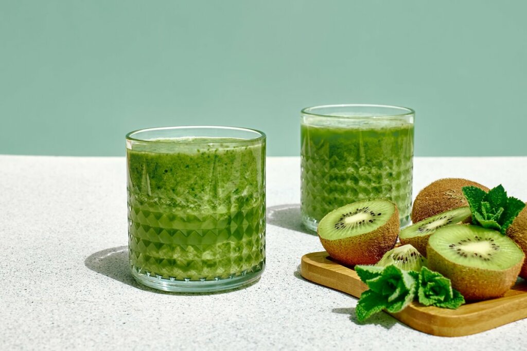 Dois copos de vidro com suco de kiwi  com couve, laranja e gengibre