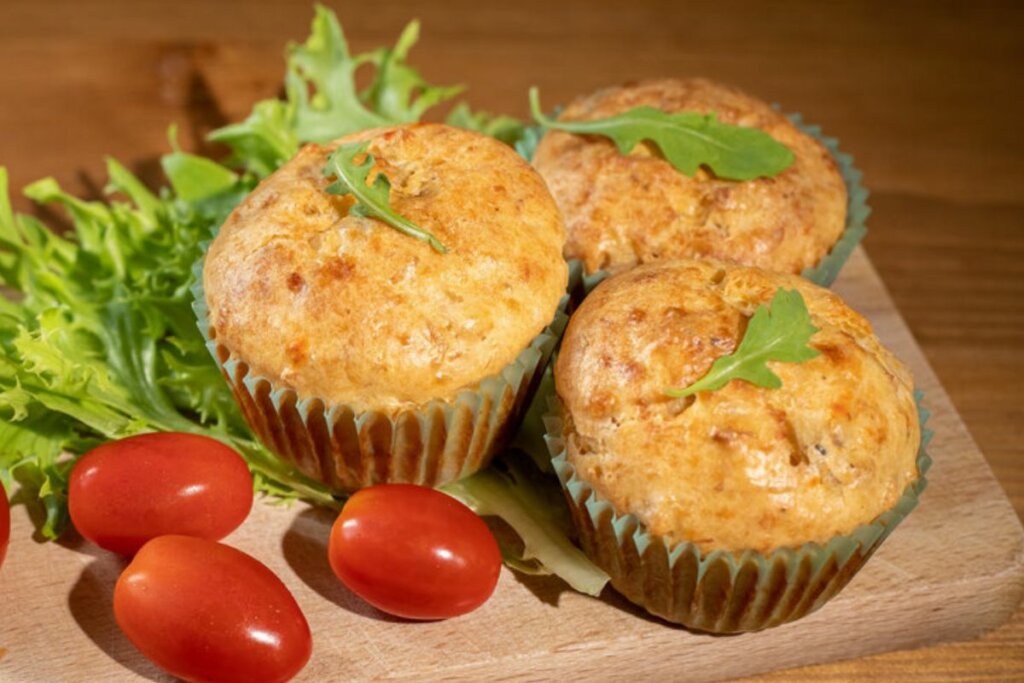 Três muffins em cima de uma tábua de madeira com tomates e alface