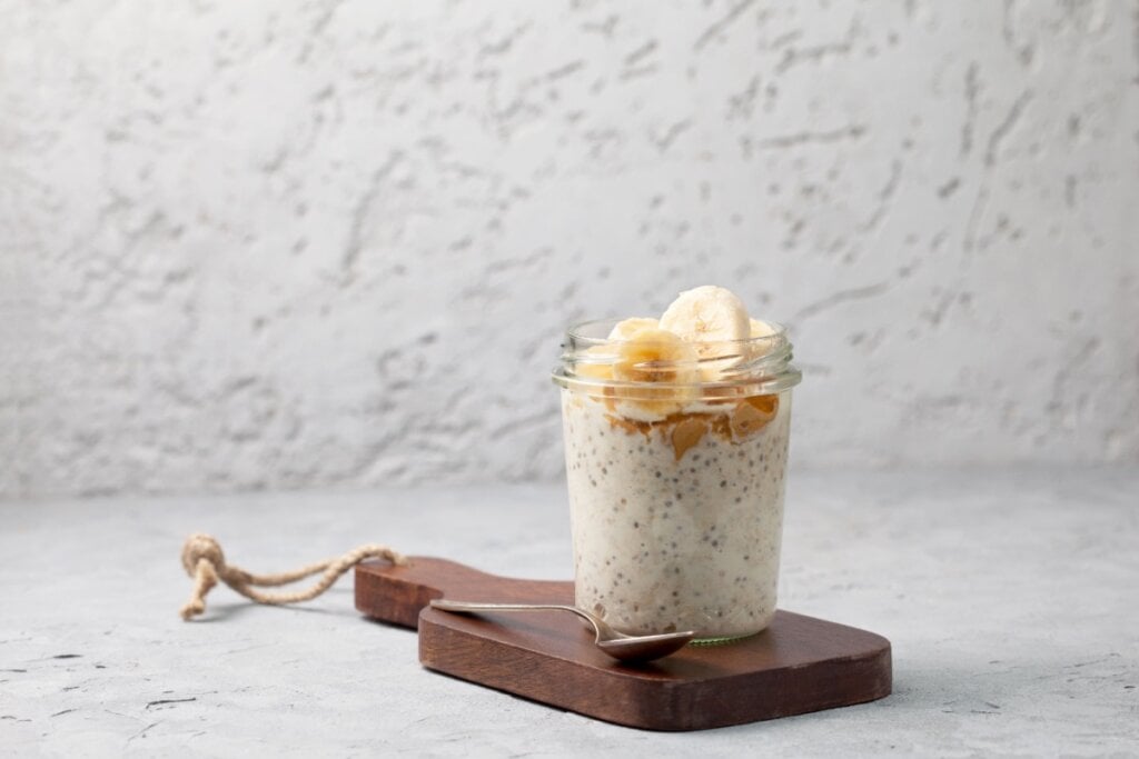 Overnight oats com sementes de chia, bananas, manteiga de amendoim, mel em um frasco de vidro sobre um fundo de concreto cinza