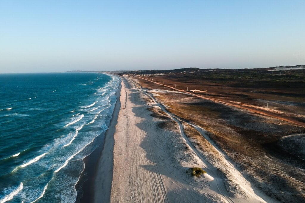 Imagem panorâmica da Praia do Japão, com um vasto litoral de areia clara, mar e uma estrada à beira da praia