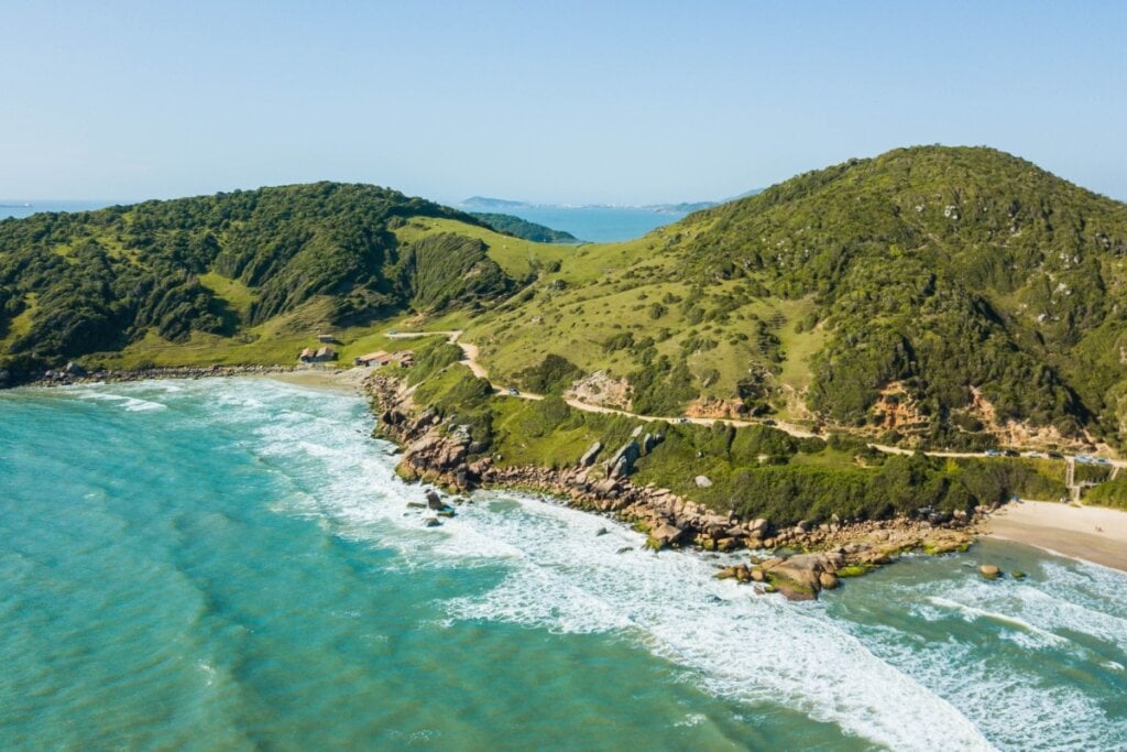 Fotografia da Praia do Rosa, cercada por montanhas verdes e mar azul com ondas