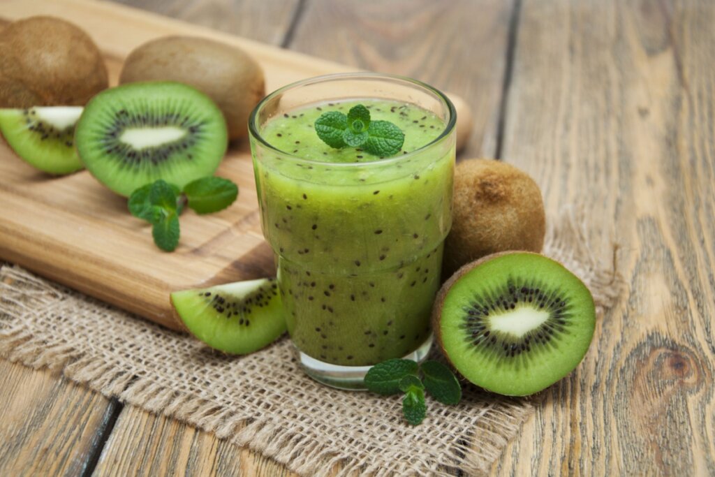 copo de vidro com suco verde de kiwi. em volta do copo há kiwis inteiros e cortados