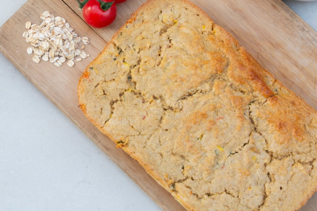 Torta de frango em cima de uma tábua de madeira com flocos de aveia e tomates