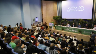 Pessoas num auditório assistindo a abertura de um evento tendo à frente a mesa de autoridades