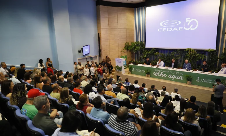 Pessoas num auditório assistindo a abertura de um evento tendo à frente a mesa de autoridades