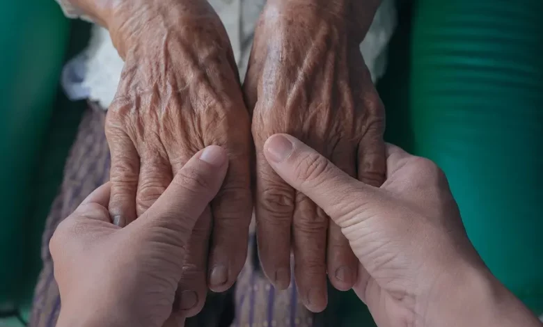 Uma pessoas segurando as mãos de uma idosa