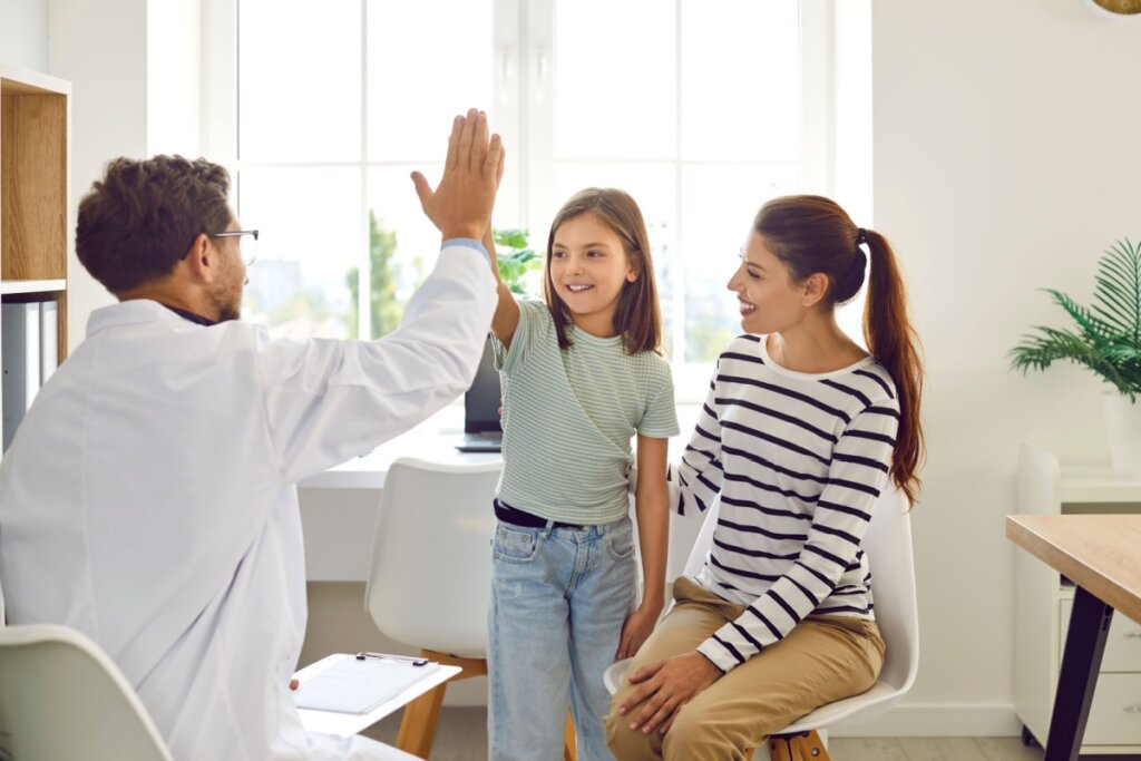 Médico fazendo um hi five com uma criança ao lado de uma mulher