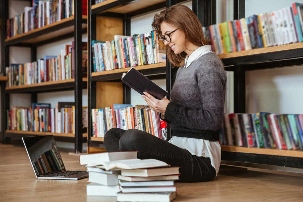 Mulher sentada em uma biblioteca lendo livro