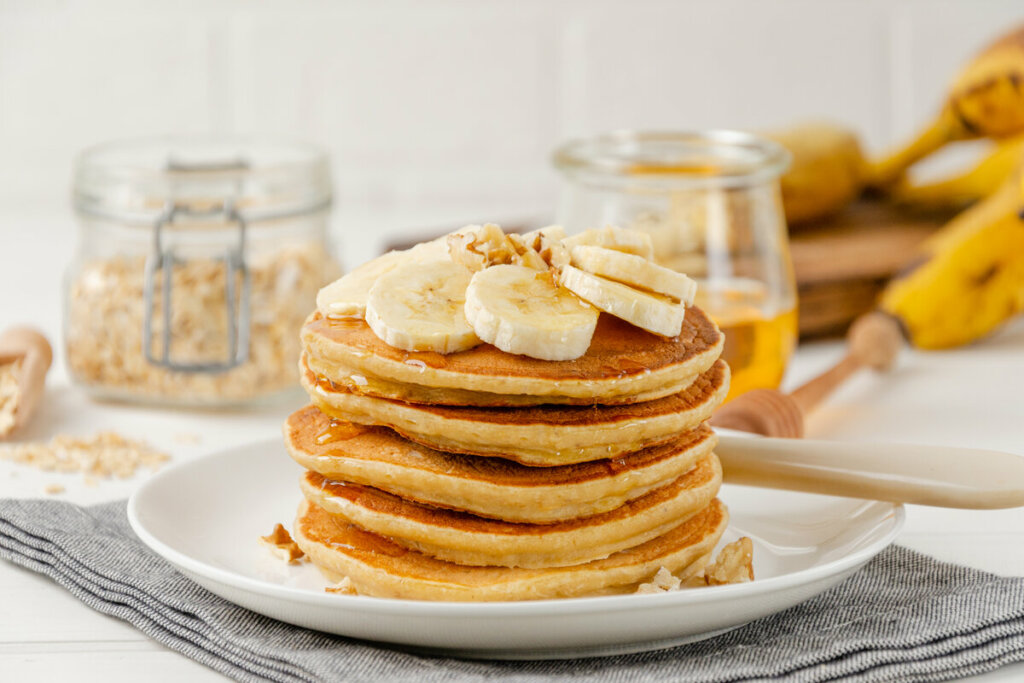 Panquecas empilhadas em cima de um prato branco e decoradas com rodelas de banana