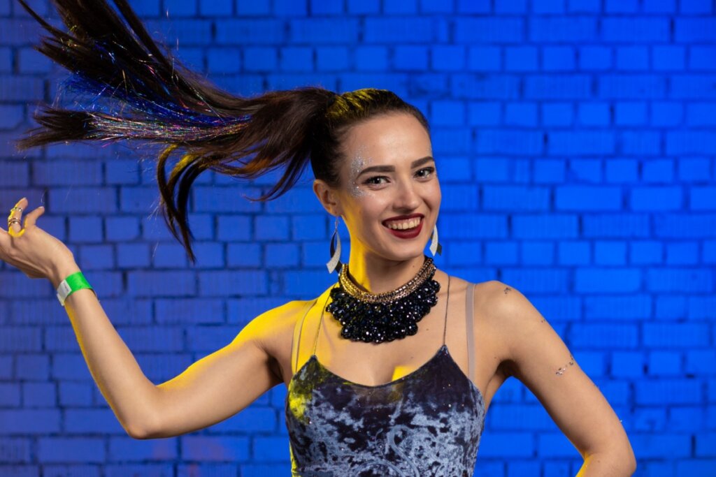 Mulher com um rabo de cavalo no cabelo, sorrindo e em frente a uma parede de tijolos com luz azul