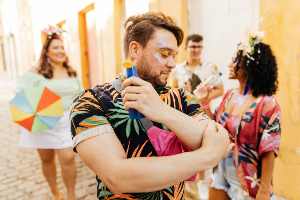 Homem usando uma camisa florida passando protetor solar no cotovelo na rua durante o Carnaval