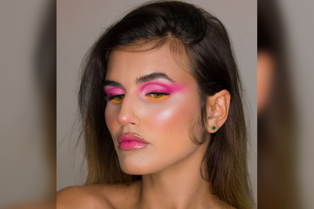 Mulher usando maquiagem com sombras coloridas rosa e máscara de cílios amarela