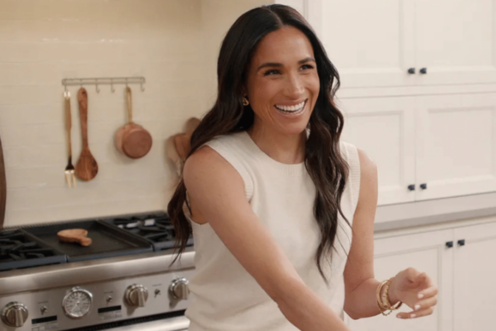 Meghan Markle em uma cozinha moderna, sorrindo enquanto prepara uma receita