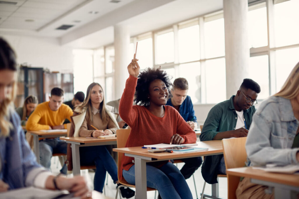 Estudante levantando a mão para fazer uma pergunta durante uma palestra na sala de aula.