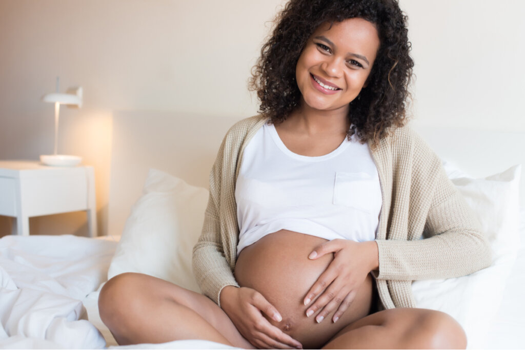 Mulher grávida deitada na cama com a mão na barriga