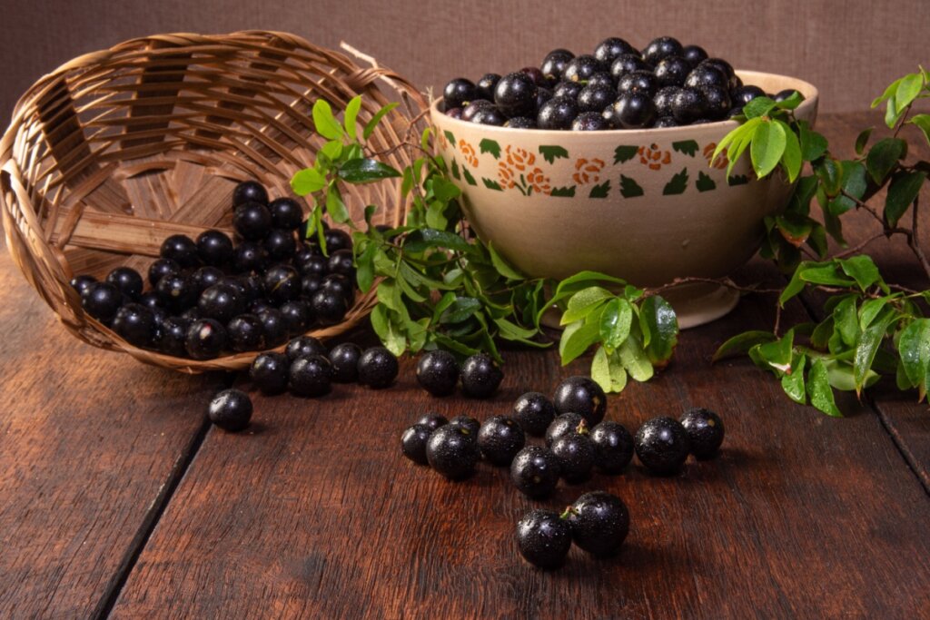 Jabuticabas frescas espalhadas sobre uma mesa de madeira rústica, com um cesto e uma tigela decorada cheios da fruta