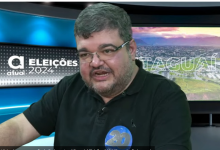 Rubão, de óculos e blusa preta, tendo ao fundo um cenário com a logomarca do jornal atual com a inscrição Eleições 2024 à esquerda e Itaguaí à direita